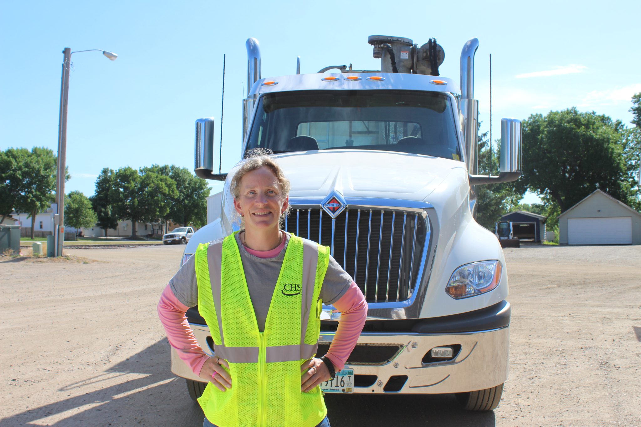 Woman standing in front of semi-truck cab while wearing a yellow safety vest