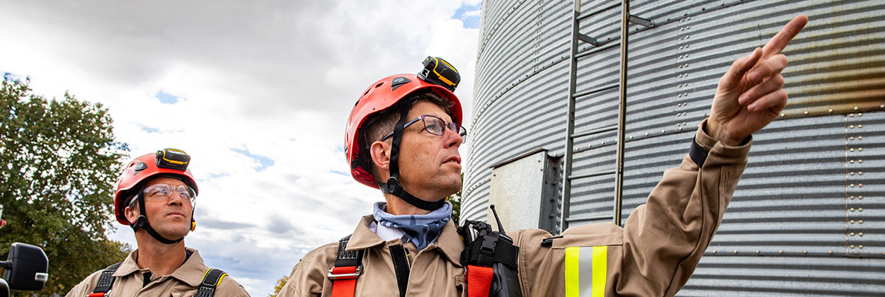 Two firefighters wearing PPE standing beside a grain bin
